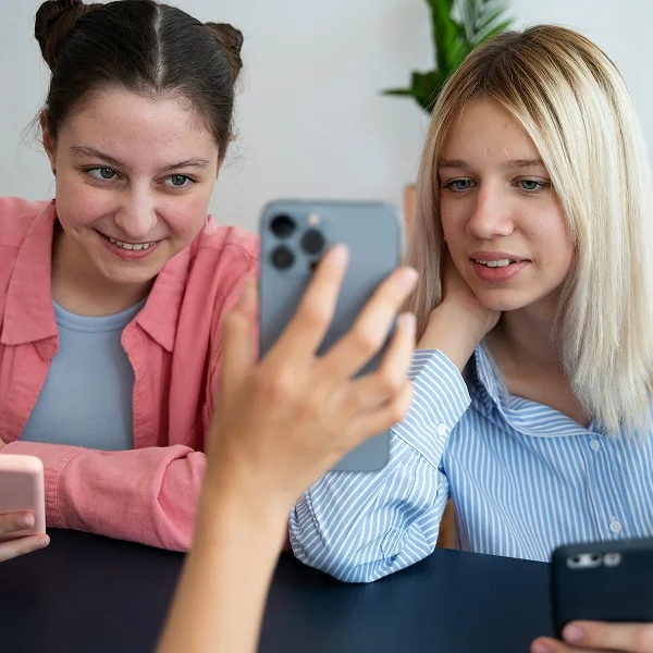 Two young women are engaged with their smartphones, sharing a moment of connection and interaction.