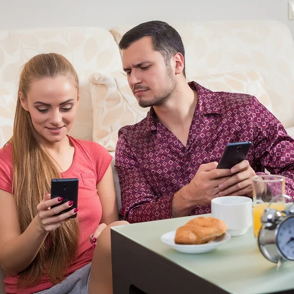 A man and woman sit on a couch, both focused on their smartphones, engaged in a shared moment of technology use.