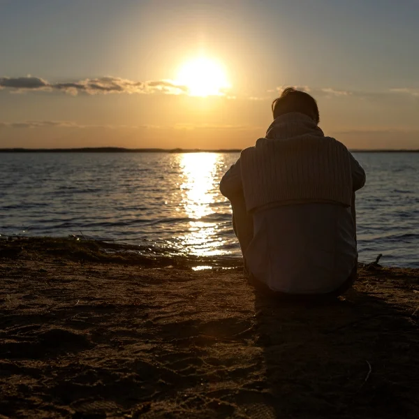 Une personne assise sur la plage, admirant le coucher de soleil aux couleurs vives.