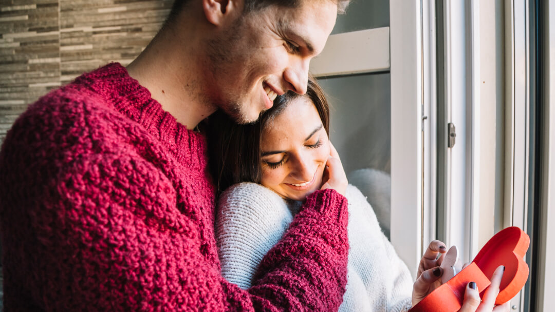 Couple amoureux s’enlaçant près d’une fenêtre, illustrant la compatibilité amoureuse comme fondement des relations durables